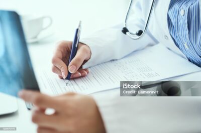 Female doctor holding x-ray or roentgen image and making notes in medical form